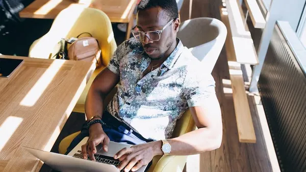An African businessman working on a laptop in a cafe — an article about website maintenance vs website redesign